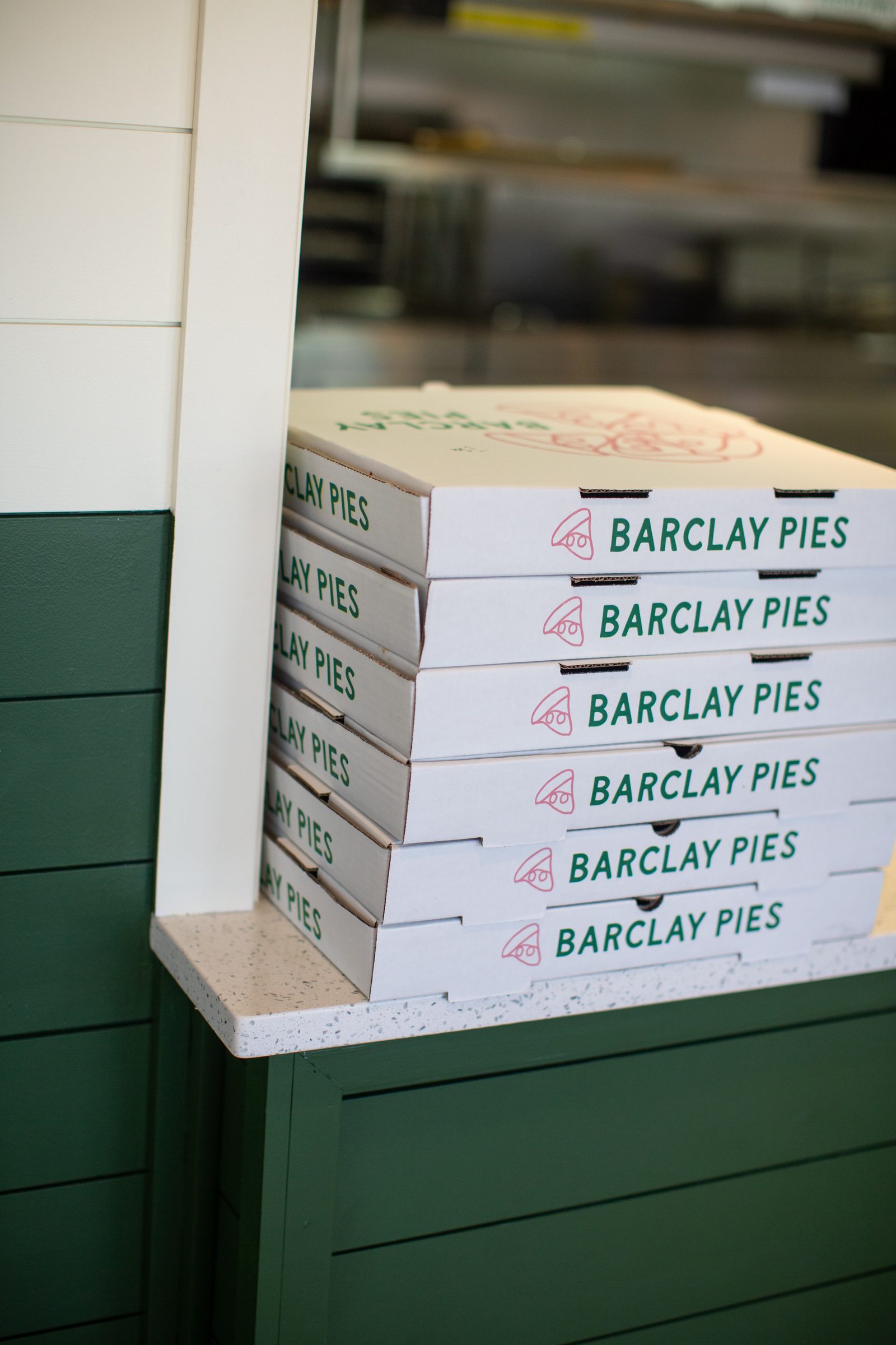 A stack of Barclay Pies pizza boxes at the counter